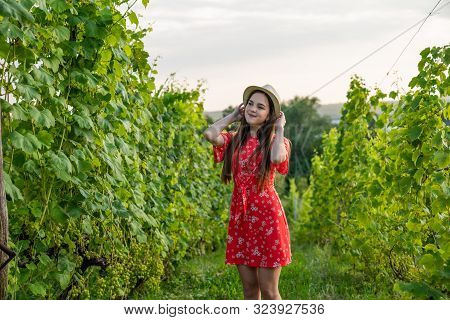 Cute Calmy Teen Girl In Red Dress And Hat Among The Vineyard, People And Garden Concept