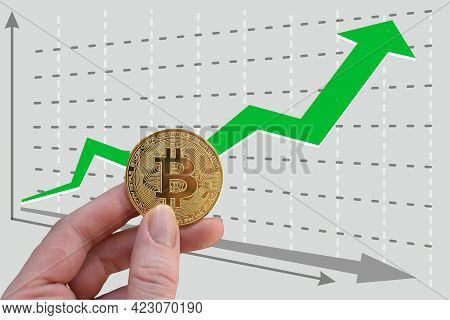 Hand Holds Bitcoin On Background Of Growing Graph With Green Upward Arrow. Exchange Rate Growth. Gre