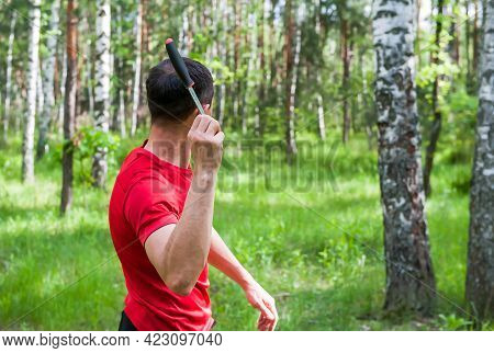 A Man Throws A Knife At A Target In The Summer Forest, Back View. Throwing A Knife