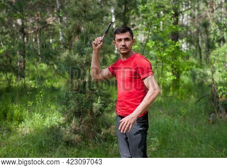 A Man Throws A Knife At A Target In The Summer Forest, Front View. Throwing A Knife