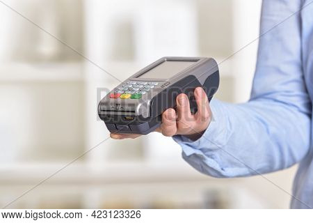 A hand holding a wireless card payment terminal at shop