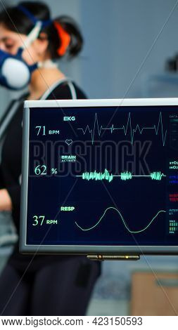 Monitor Showing Ekg Scan Of Athlete Running On Cross Trainer And Medical Specialists Supervise Exerc