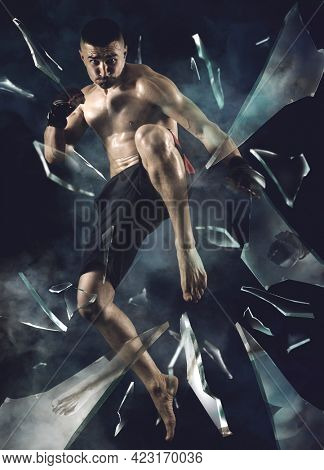 MMA male fighter jumping with a knee kick. Shards of broken glass background
