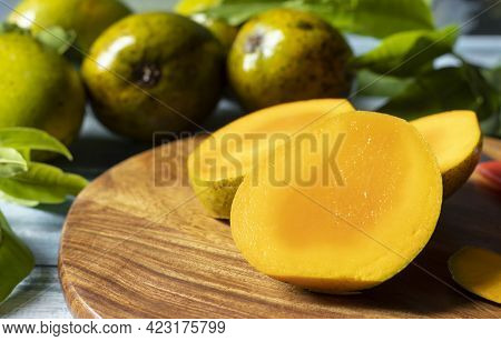 Selective Focus On Ripe Mango Slices On Wooden Chopping Board Along With Mangoes And Leaves On Woode