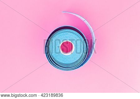 Blue Roll Of Kinesiology Tape On Pink Background, Flat Lay. Recovery, Anti-aging Procedures Concept.