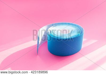 Close Up Blue Roll Of Kinesiology Tape On Pink Background With Trendy Sun Light And Shadows. Recover