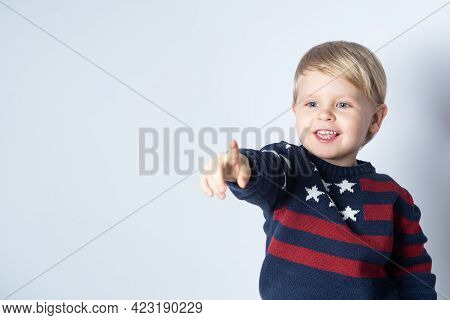 Smiling Child In A Sweater With An American Flag Is Showing Something On A White Background With A C