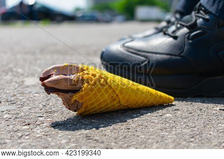 A Man Threw A Tasteless Chocolate Ice Cream In A Waffle Cone On The Asphalt Under His Feet, Taking A