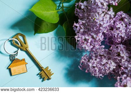 House Key With Keychain On Blue Spring Background And Lilac Branches.summer Holiday Home, Booking Co