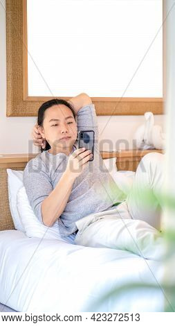 Relaxing And Happy Asian Man Long Hair Lay On The Bed And Play Mobile In The Morning Time.