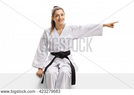 Woman in kimono and black belt sitting on a panel and pointing to the side isolated on white background