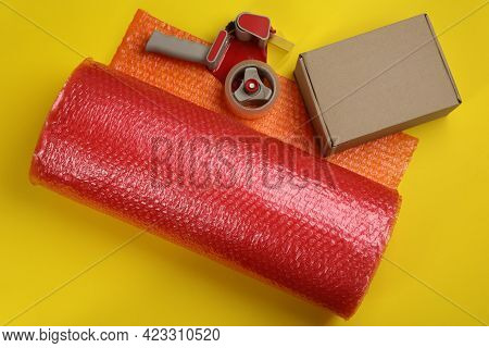 Bubble Wrap Roll, Cardboard Box And Tape Dispenser On Yellow Background, Flat Lay