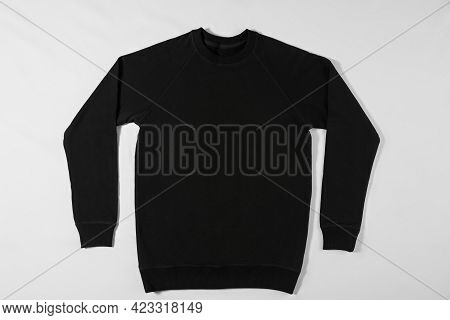 Black Raglan Lying On A White Background In The Studio. Classic Clothing Concept. Blank Sweater With