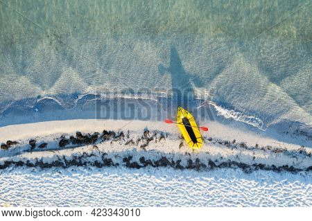 Yellow packraft rubber boat with red padle and turquoise water waves from top view. Beach with yellow sand glowing by sunlight. Travel summer vacations seascape background from drone