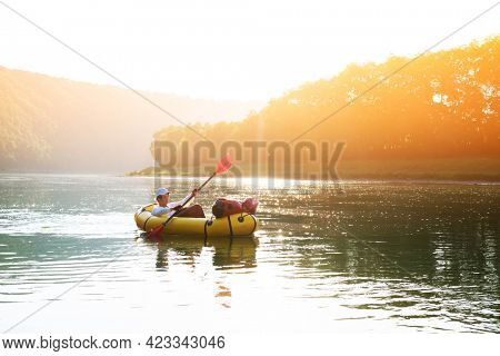 Tourist on yellow packraft rubber boat with red padle on a sunrise river. Packrafting. Active lifestile concept