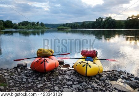 Orange and yellow packrafts rubber boats with padles ready for adventures on a sunrise river. Packrafting. Active lifestile concept