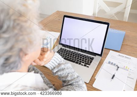 Mixed race senior woman sitting at table making video call using laptop. staying at home in isolation during quarantine lockdown.