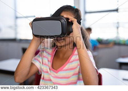 African american girl wearing vr headset while sitting on her desk in the class at school. school and education concept