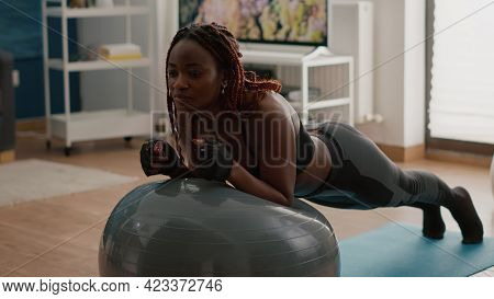 African Slim Woman Streching Abdominal Muscle While Sitting On Yoga Swiss Ball Doing Morning Workout