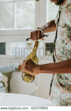 Black man uncorking a white wine bottle