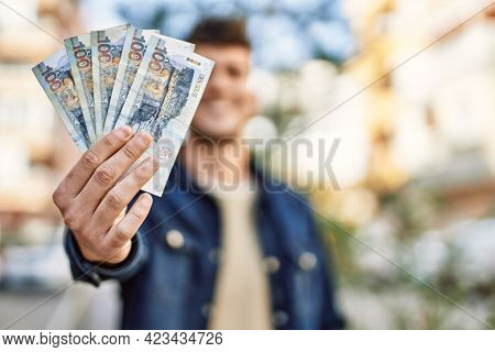 Young hispanic man smiling happy holding peruvian sol banknotes at the city