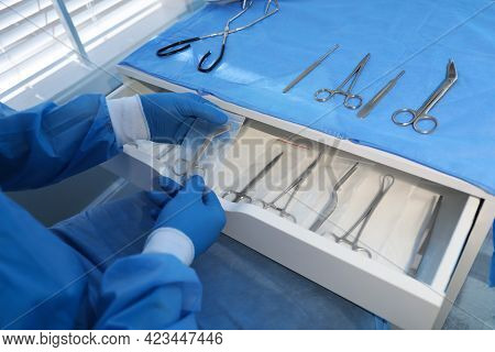 Doctor Putting Pott's Scissors Into Drawer Indoors, Closeup. Table With Different Surgical Instrumen