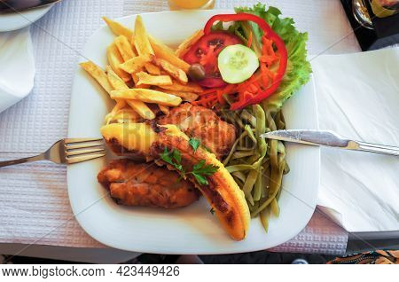 Fish espada with fried banana, french potatoes, kidney beans and fresh vegetables. Traditional Madeira dish. Top view.  