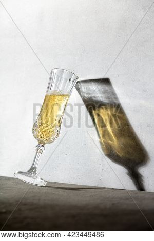 Champagne glass and long glass shadow against concrete wall. Modern still life with hard shadows. Summer drink concept