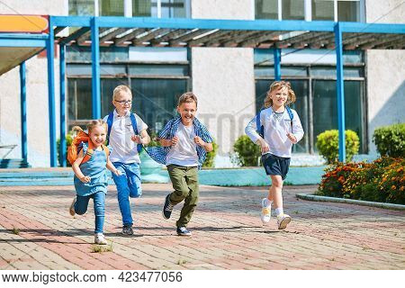 Group Of School Children With Backpacks Run Out Of School, After The End Of Classes. Classmates, Sch