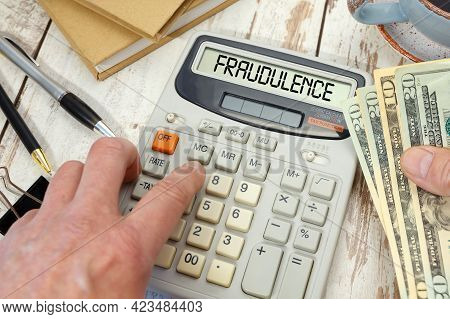 Money In Hand Next To A Calculator And Office Supplies. Fraudulence - Word On Calculator.