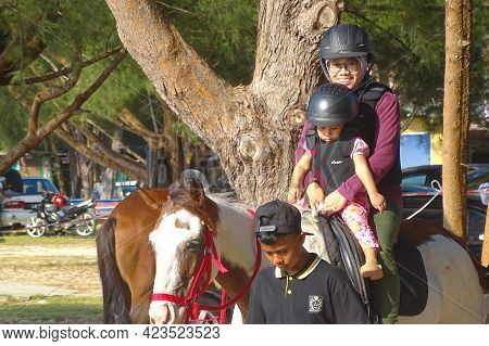 Labuan,malaysia-sept 1,2019:young Smiling Woman Mother And Small Daughter Sitting On Horse And Ridin