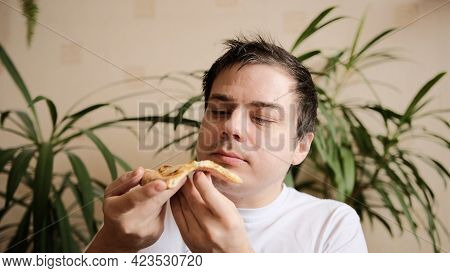 The Young Man Takes A Slice Of Pizza, Takes A Bite With Passion And Chews It. The Guy Looks At A Sli