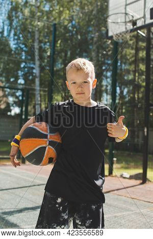 Stylish Sportive Little Kid Boy With Basketball Ball Shows Thumb Up Gesture In Sunlight. Healthy Chi