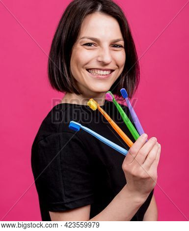 Beautiful Happy Young Woman With Different Colored Toothbrushes On Blank Pink Background