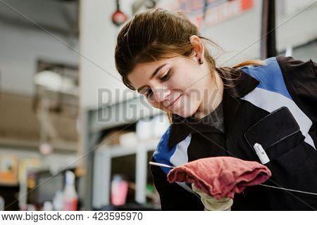 Young female mechanic wiping the engine oil dipstick