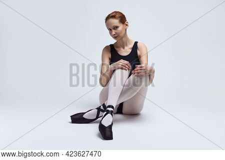 Sensual Professional Female Ballet Dancer In Body Suit Posing With Legs Folded White On Floor.
