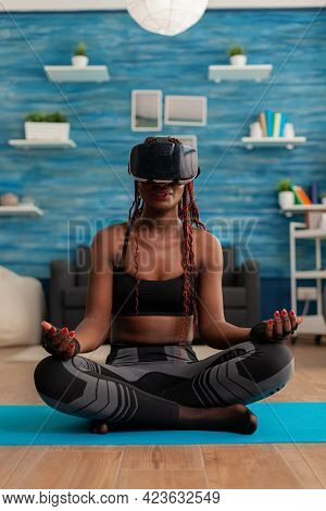 Black Woman Experiencing Virtual Reality Training Body And Mind Meditating In Lotus Pose Sitting On 
