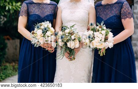 Bride And Bridesmaids In Identical Blue Dresses Are Standing Side By Side And Holding Bouquets In Th