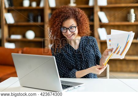Virtuel Conference. Female Office Employee Sitting At Office Desk In Front Of The Laptop And Showing