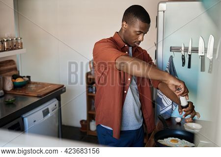 Young African Man Adding Salt To Eggs In A Frypan