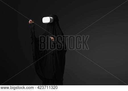 Muslim Nun In Black Abaya Gesturing In Vr Headset Isolated On Black