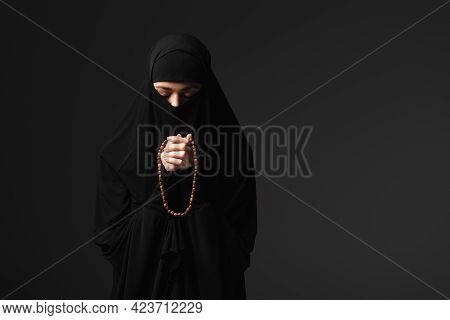 Muslim Nun In Black Traditional Clothing Praying With Rosary Isolated On Black