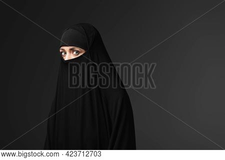 Young Muslim Woman In Black Traditional Clothing Looking At Camera Isolated On Black