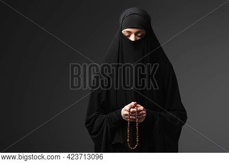 Muslim Woman In Black Niqab Praying With Rosary Isolated On Black