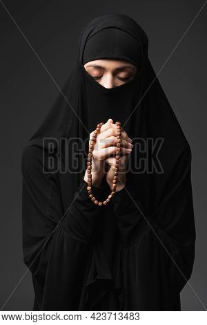 Young Muslim Woman With Closed Eyes Holding Rosary While Praying Isolated On Black