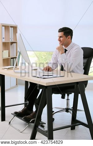 Man Using Footrest While Working On Computer In Office