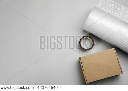 Bubble Wrap Roll, Cardboard Box And Tape On Light Background, Flat Lay. Space For Text