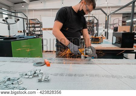 Heavy Industry Engineering Factory Interior with Industrial Worker Using Angle Grinder and Cutting a Metal Tube.He Wears a Mask on His Face Because of the Coronavirus Pandemic