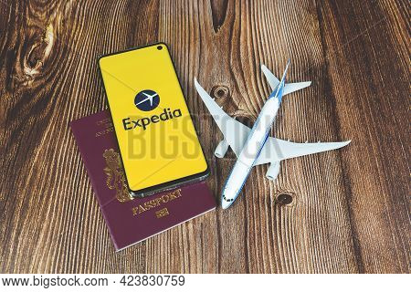 Swansea, Uk - June 3, 2021: Smartphone With Expedia App Logo With Plane Toy And Red Passport On Wood