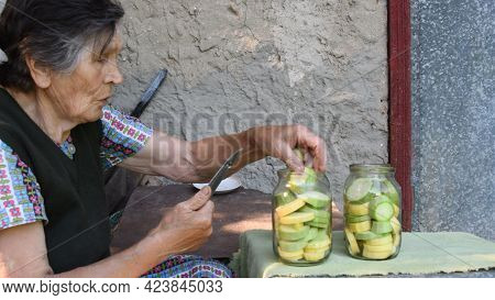 80s Mixed Race Senior Woman Place Zucchini Slices Into Jars As Preservation. Granny Make Homemade Ca